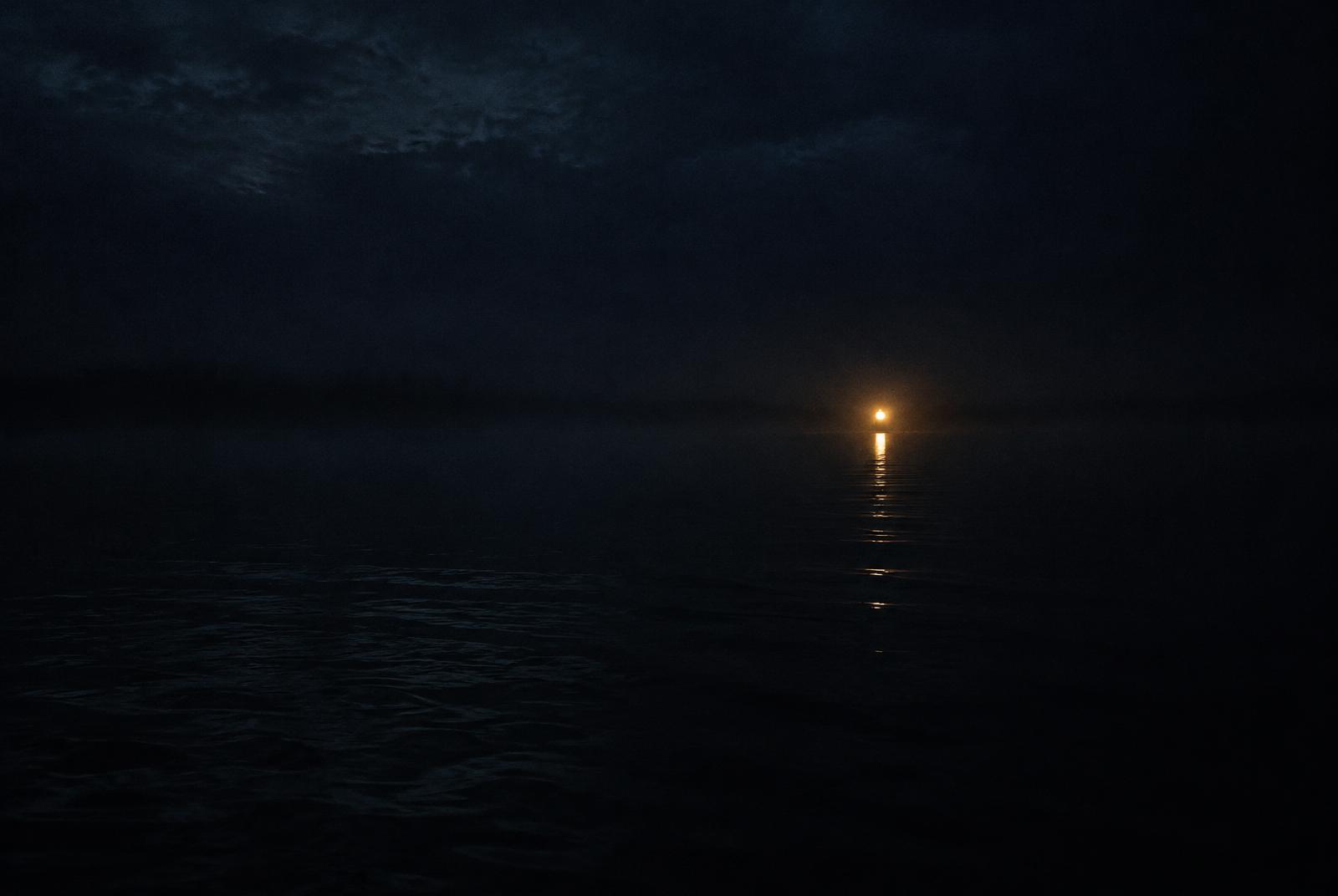 A single distant lantern light glowing across dark water at night
